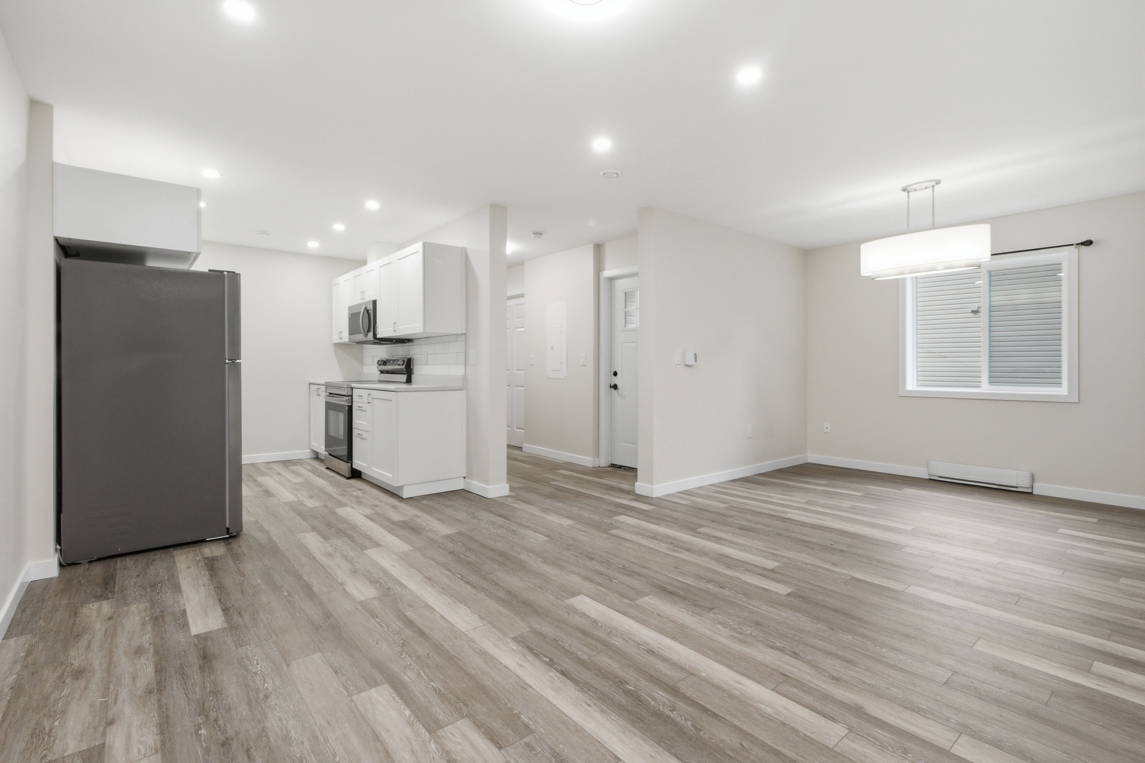 Open living and kitchen layout with a stainless refrigerator, a dining nook, and a drum pendant by the window