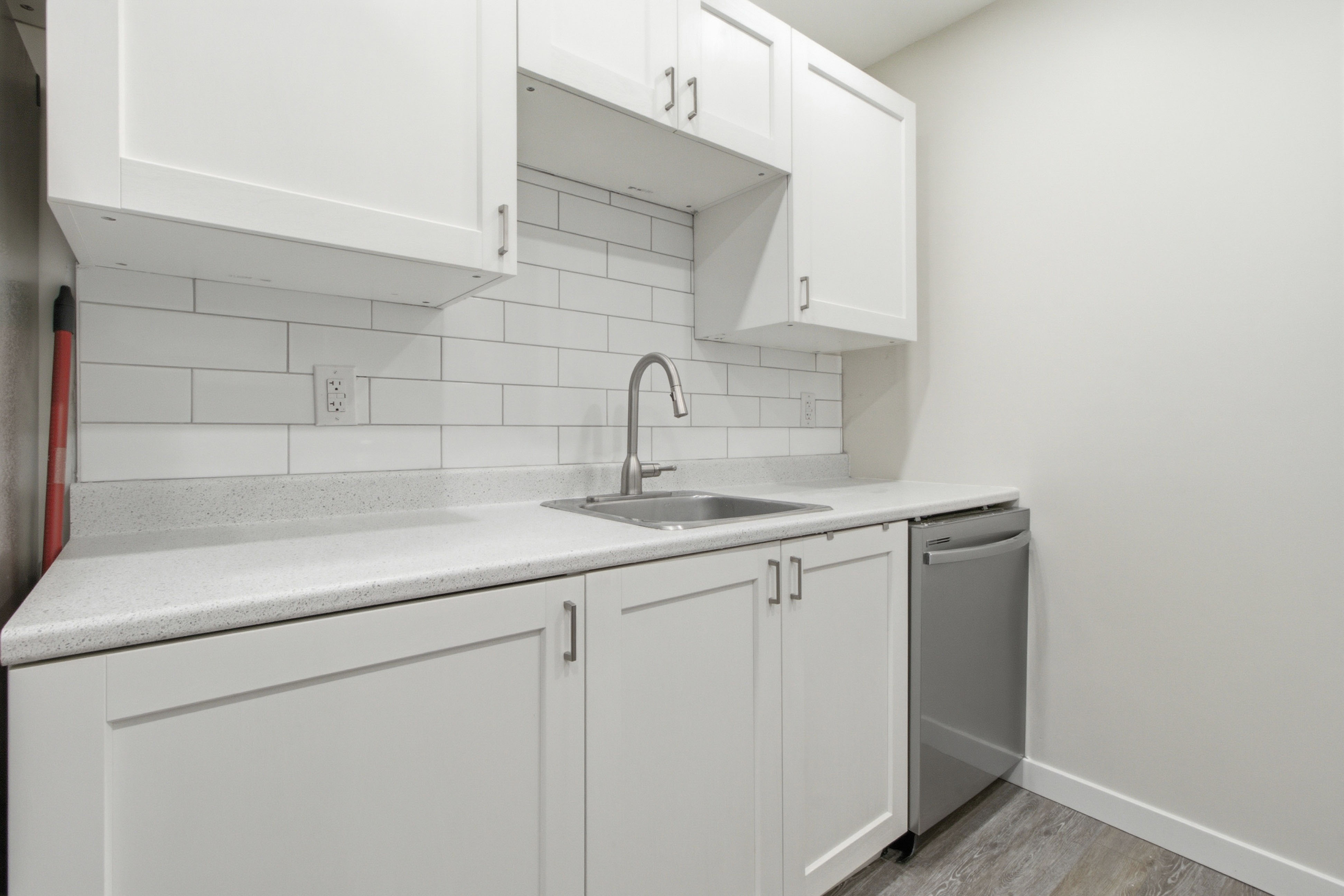 Kitchen run with quartz-look counters, a stainless sink, white shaker cabinets, and a built-in dishwasher