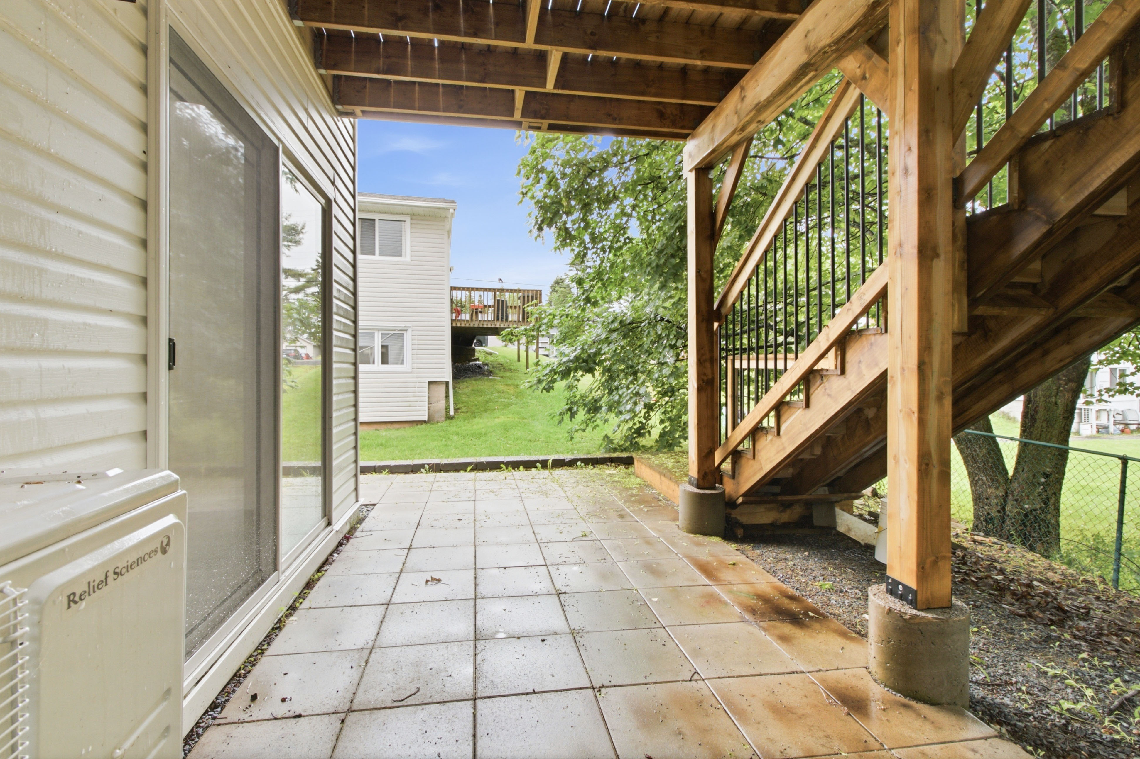 Hayes Rentals exterior — paved patio, wood deck, and a grassy yard backing onto trees