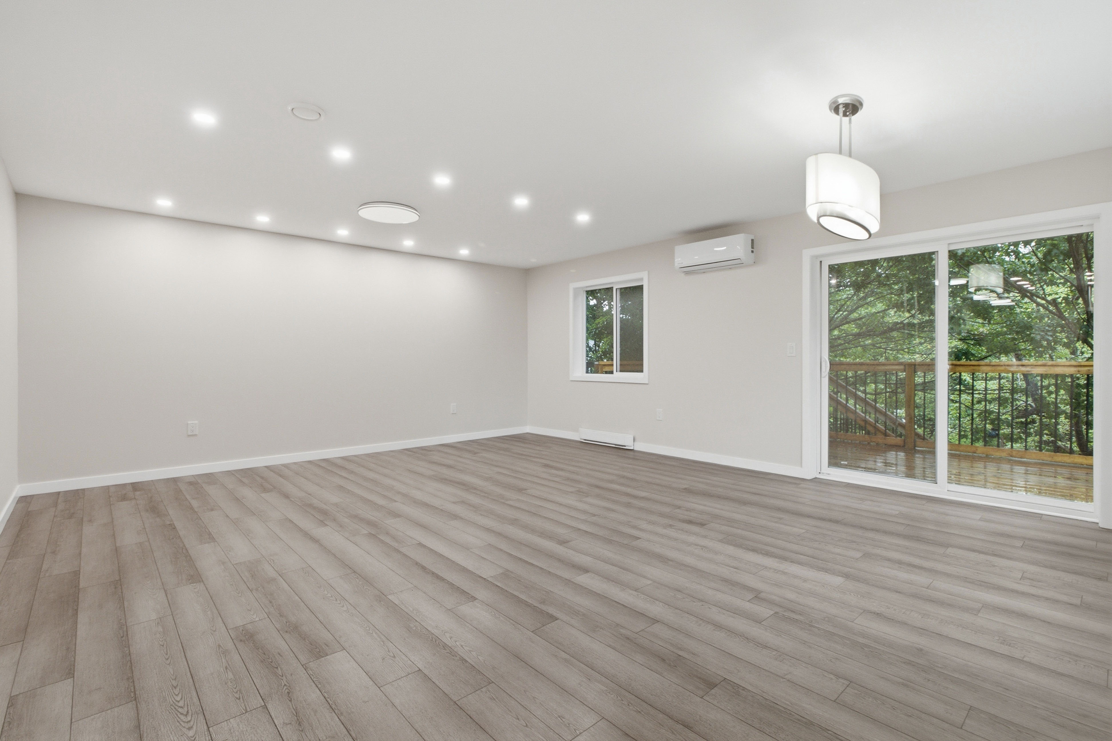 Generous living room with two windows, a sliding glass door to the deck, and a treed outlook