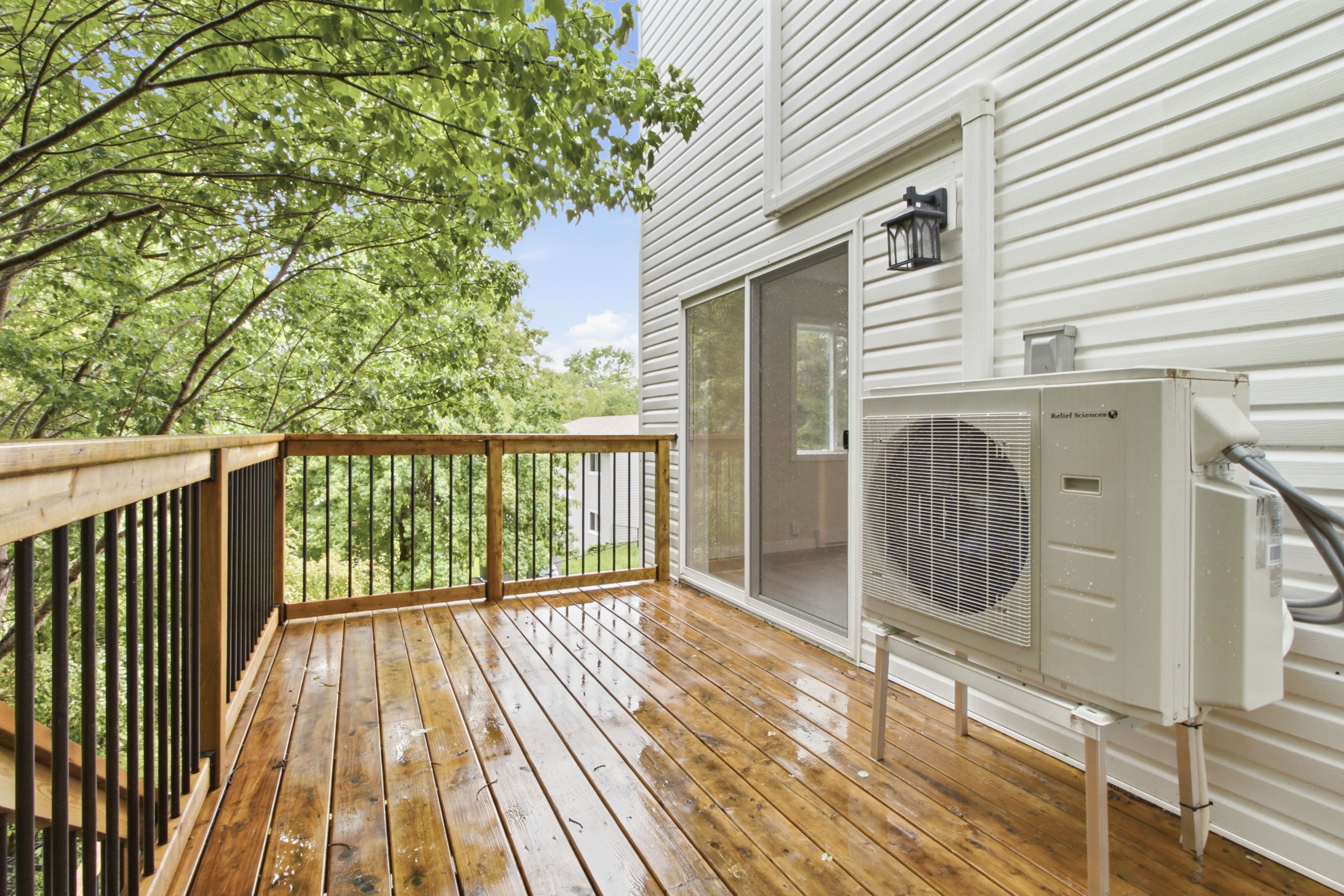 Sunlit wood deck with a heat-pump condenser and treetop views